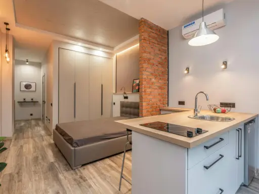 Aménagement studio 25 m2 : lit, cuisine équipée, rangements intégrés, mur en briques apparentes. Style moderne et fonctionnel.