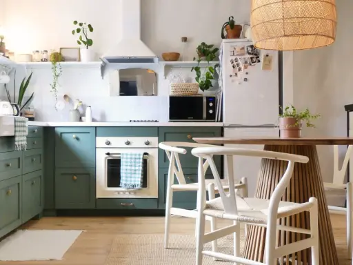 Cuisine verte avec four blanc, îlot central en bois et chaises blanches. Un modèle de cuisine simple et chaleureux.