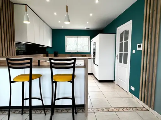 Cuisine moderne aux murs bleu canard, îlot central en bois, tabourets jaunes vifs. Une véritable inspiration cuisine pour des repas conviviaux.