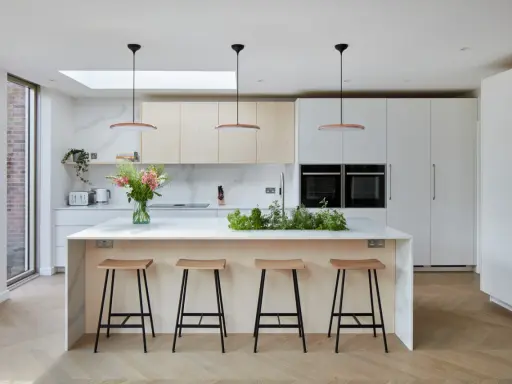 Élégante cuisine ouverte avec îlot central, tabourets en bois, et un jardin d'herbes aromatiques. Des armoires blanches et des fours intégrés complètent ce design moderne.