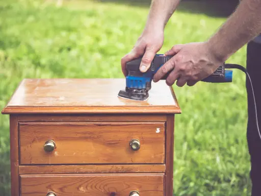 Préparation d'un meuble en bois : ponçage pour comment décaper un meuble en bois foncé. L'outil électrique enlève l'ancienne finition.