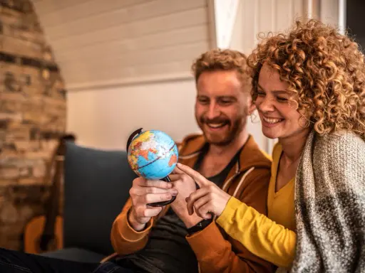 Couple souriant planifiant leur déménagement à l'étranger, pointant du doigt un globe terrestre.