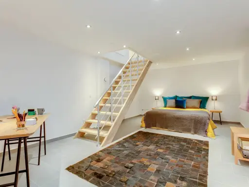 Aménager un sous-sol en pièce habitable : un lit douillet, un bureau fonctionnel et un escalier moderne créent un espace de vie confortable.