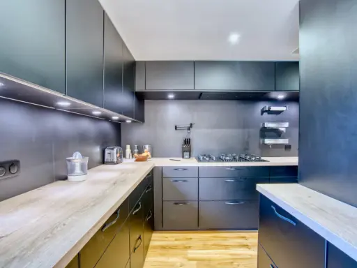 Cuisine moderne aux armoires sombres et plans de travail en bois. Une plaque de cuisson est installée, créant une cuisine sans hotte visible.