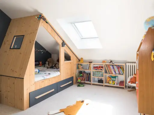 Chambre d'enfant aménagée sous les combles avec un lit cabane en bois, étagères remplies de jouets et livres. Un plan d'aménagement astucieux pour optimiser l'espace.