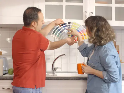 Un couple choisit des couleurs pour peindre le carrelage de sa cuisine, tenant un éventail de nuanciers.