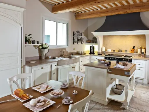 Cuisine de maison provençale avec poutres apparentes, évier en pierre, et table dressée pour un goûter gourmand.