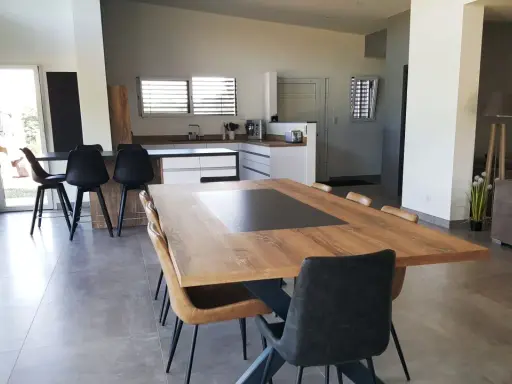 Grande cuisine ouverte sur salon, avec îlot central, table en bois et chaises modernes.