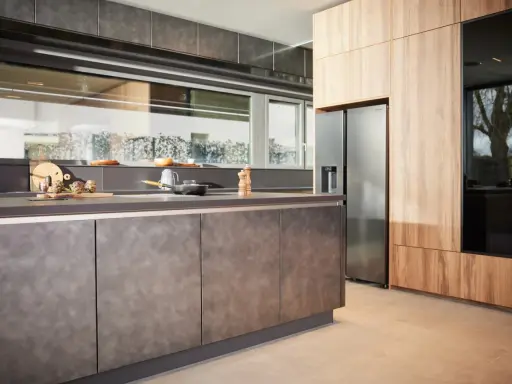 Une cuisine en plan moderne avec des armoires en bois et des surfaces sombres. Un réfrigérateur en acier inoxydable est visible.