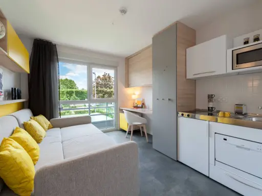 Aménagement studio moderne avec canapé, coin cuisine, bureau et vue sur jardin.