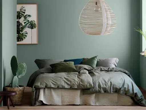 Une chambre vert sauge apaisante avec un lit douillet, un cactus et une œuvre d'art botanique.