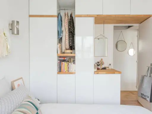 Chambre avec dressing intégré, organisée avec des étagères de livres et des vêtements suspendus. Un coin coiffeuse avec miroir et accessoires complète l'espace.