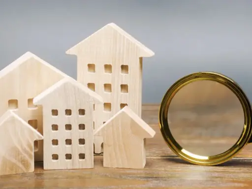 Maquettes de maisons en bois et une loupe, symbolisant la recherche pour trouver un logement rapidement.