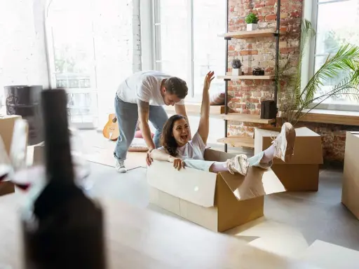 Un couple s'amuse en déménageant. Elle glisse dans un carton, un objet fragile, tandis qu'il la pousse.
