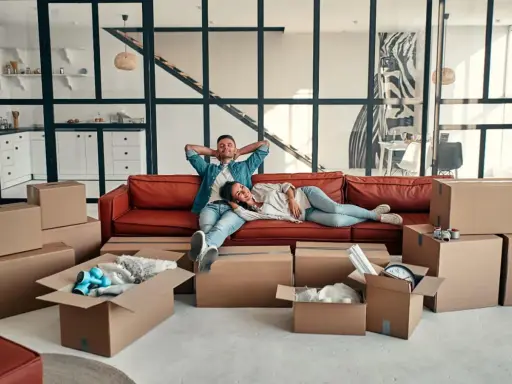 Couple se repose sur un canapé rouge entouré de cartons, signe d'un emménagement appartement réussi.