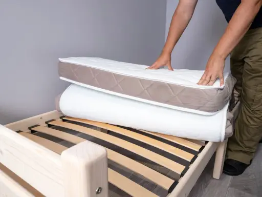 Un homme montre comment plier un matelas sur un sommier en bois.