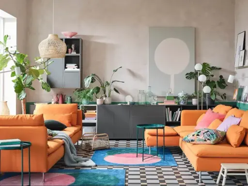 Deux canapés orange vif dans un salon moderne avec des plantes, un tapis coloré et un mur vert.