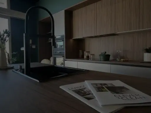 Cuisine moderne avec îlot central, robinetterie noire et magazines sur le plan de travail. Idéal pour rénover une cuisine.
