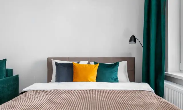 Lit de chambre cabine avec coussins colorés et rideaux verts.