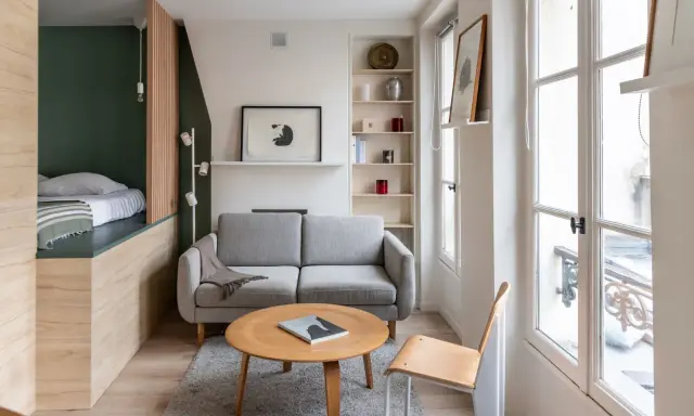 Aménagement intérieur appartement : un salon cosy avec canapé gris, table basse en bois, et un lit surélevé dans un coin.