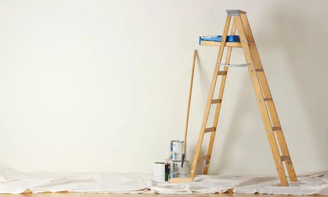 Préparation pour peindre une chambre : échelle en bois, pots de peinture, rouleau et bâton sur une toile de protection.