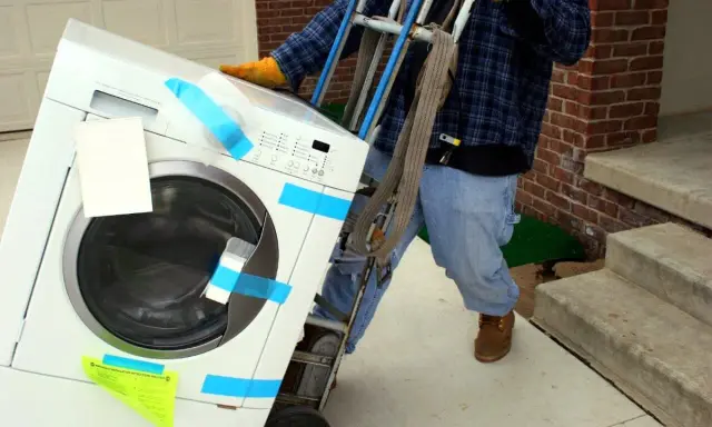 Un homme utilise un chariot pour comment monter une machine à laver dans les escaliers.