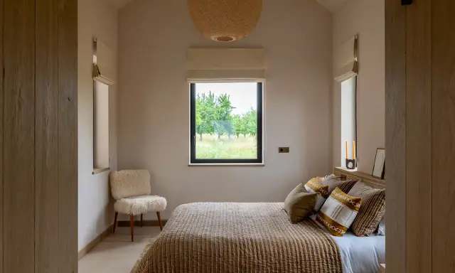 Aménagement petite chambre cosy avec lit douillet, fauteuil mouton et vue sur la nature.