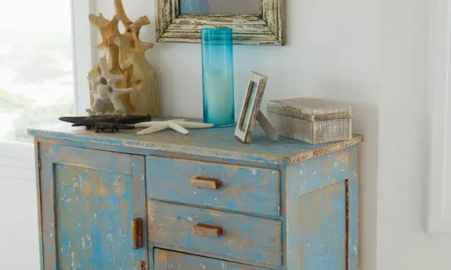 Meuble patiné bleu délavé, orné d'objets marins et d'une boîte décorative.
