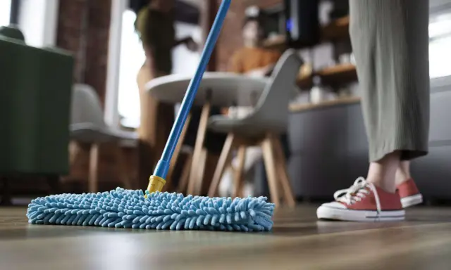 Nettoyage avant déménagement : une personne passe une serpillère bleue sur un parquet.