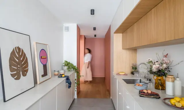 Cuisine moderne et lumineuse avec îlot central, décoration murale et personne marchant au fond.
