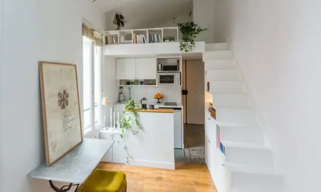 Un petit appartement optimisé avec une cuisine, un coin repas et un lit en mezzanine accessible par des escaliers blancs.