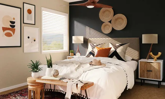 Une chambre moderne avec une décoration murale en vannerie, des tableaux abstraits et un ventilateur de plafond. Le lit est fait de blanc, avec des coussins graphiques et une touche de couleur ocre.