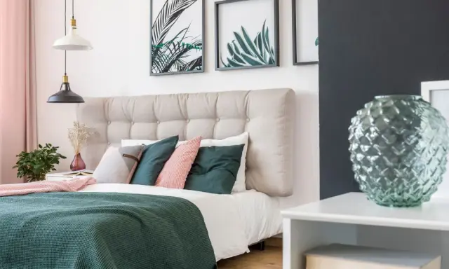 Une belle idée de tête de lit capitonnée, avec des coussins verts et roses, des plantes et des cadres botaniques.