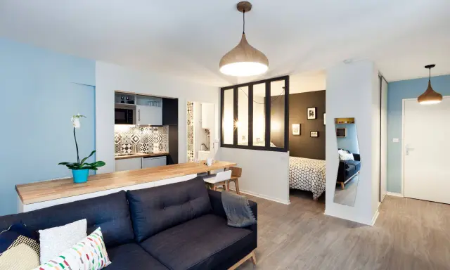 Aménagement studio 30m2 : salon cosy, cuisine moderne, coin repas et chambre séparée par une verrière.