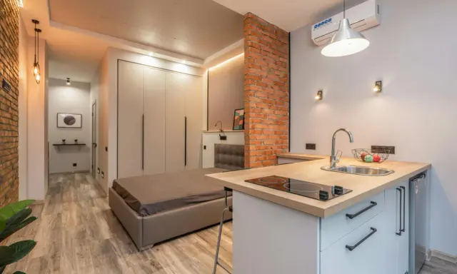 Aménagement studio 25 m2 : lit, cuisine équipée, rangements intégrés, mur en briques apparentes. Style moderne et fonctionnel.