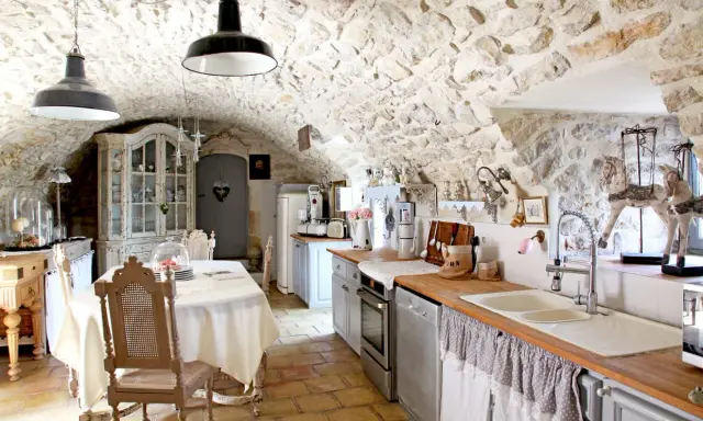Cuisine rustique avec des vieux meubles patinés, un buffet ancien, une table dressée et des murs en pierre.