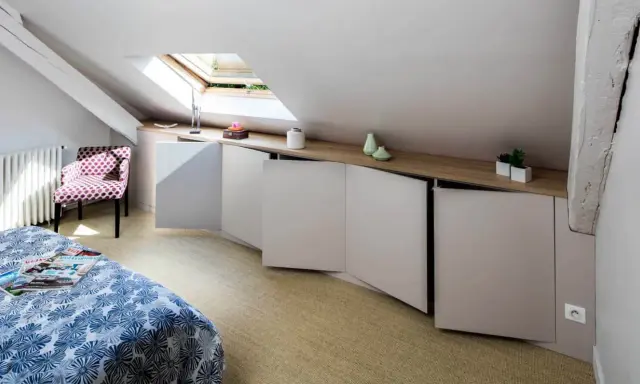 Chambre mansardée d'un coté avec lit, fauteuil à pois et rangements bas sur mesure. Un velux éclaire la pièce.