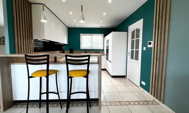 Cuisine moderne aux murs bleu canard, îlot central en bois, tabourets jaunes vifs. Une véritable inspiration cuisine pour des repas conviviaux.