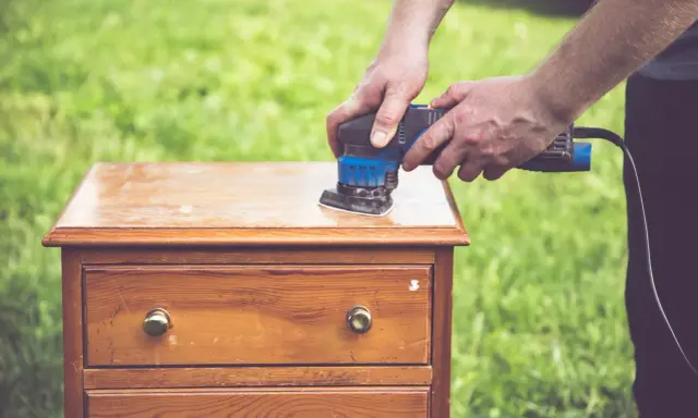 Préparation d'un meuble en bois : ponçage pour comment décaper un meuble en bois foncé. L'outil électrique enlève l'ancienne finition.