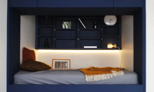 Un lit confortable dans une alcôve bleue, avec des étagères remplies d'objets décoratifs. Parfait pour refaire sa chambre avec style.
