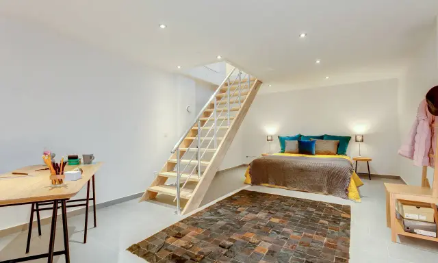 Aménager un sous-sol en pièce habitable : un lit douillet, un bureau fonctionnel et un escalier moderne créent un espace de vie confortable.