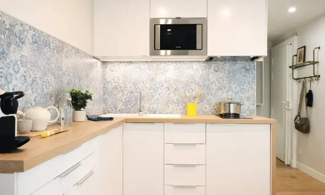 Cuisine moderne avec crédence carrelée bleu et blanc, plans de travail en bois et meubles blancs. Une idée pour une crédence cuisine blanche et originale.