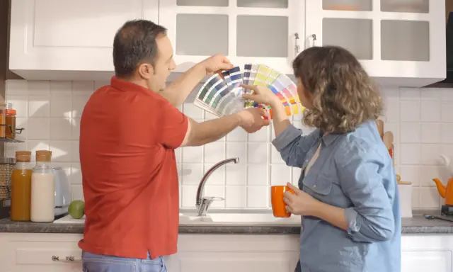 Un couple choisit des couleurs pour peindre le carrelage de sa cuisine, tenant un éventail de nuanciers.