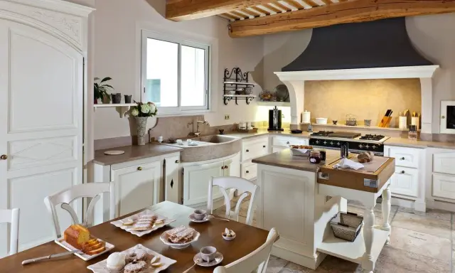 Cuisine de maison provençale avec poutres apparentes, évier en pierre, et table dressée pour un goûter gourmand.