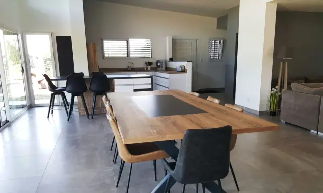 Grande cuisine ouverte sur salon, avec îlot central, table en bois et chaises modernes.