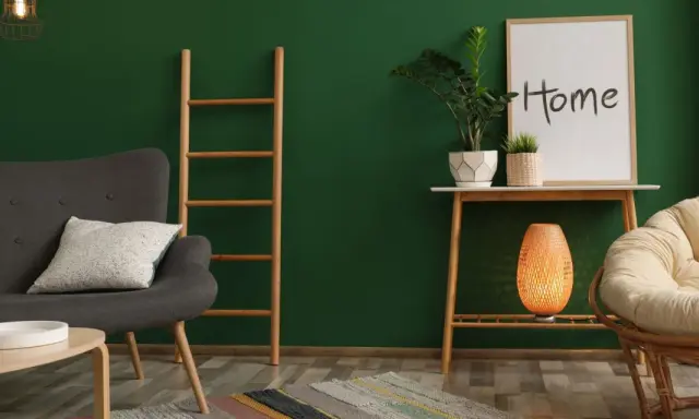 Un salon cosy avec un mur vert sapin, un fauteuil gris, une échelle en bois, une plante et un cadre "Home".