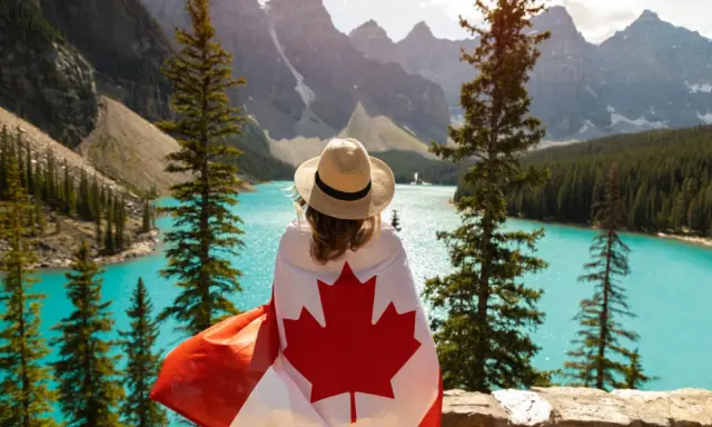 Vue d'une femme avec un drapeau canadien sur les épaules, contemplant un lac turquoise et des montagnes. Un rêve de déménagement France Canada.