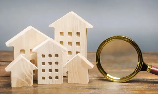 Maquettes de maisons en bois et une loupe, symbolisant la recherche pour trouver un logement rapidement.