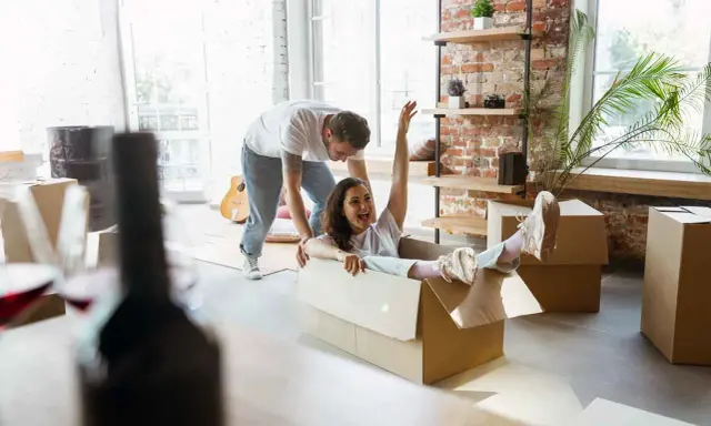 Un couple s'amuse en déménageant. Elle glisse dans un carton, un objet fragile, tandis qu'il la pousse.