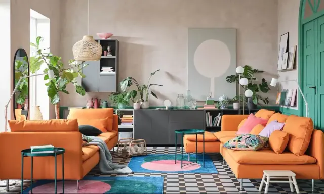 Deux canapés orange vif dans un salon moderne avec des plantes, un tapis coloré et un mur vert.